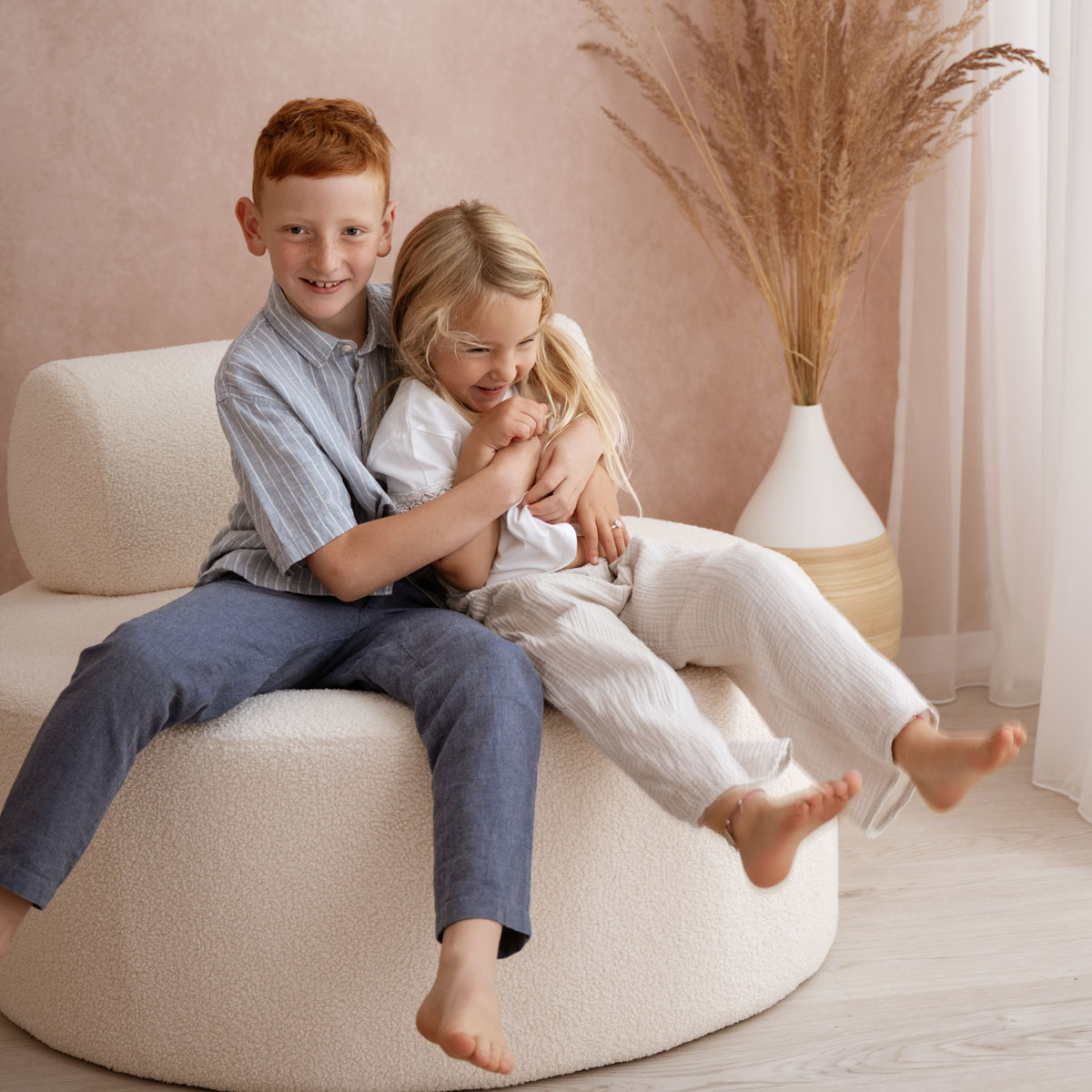 Bruder und Schwester sitzen lachend auf einem Hocker