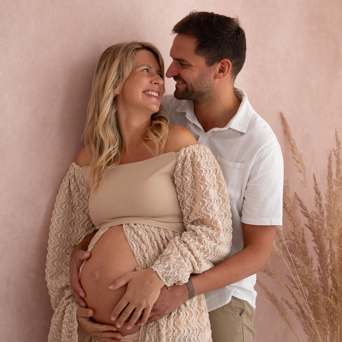 Werdende Eltern halten gemeinsam den Babybauch und lächeln sich an