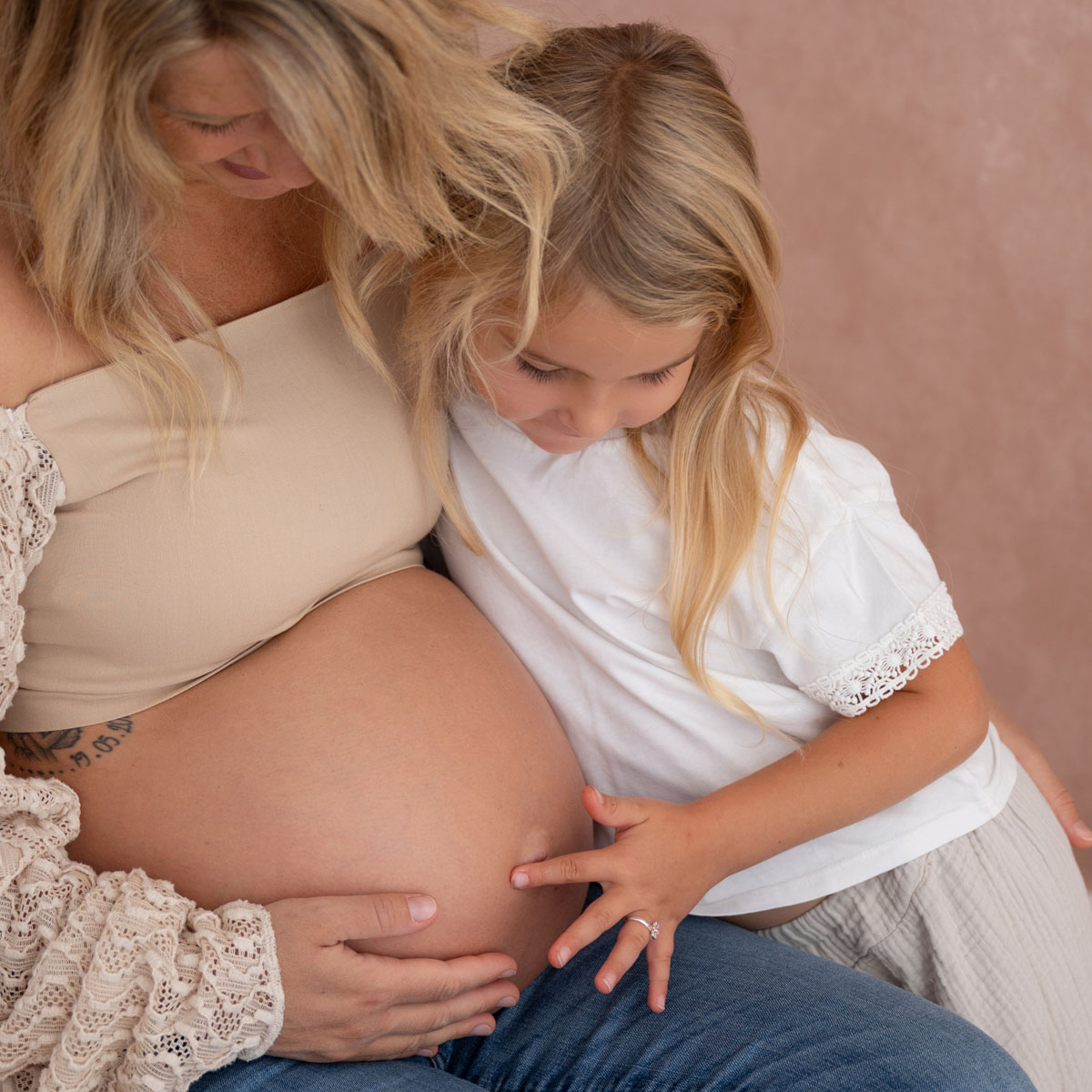 Kind kuschelt sich an den Babybauch der Mama