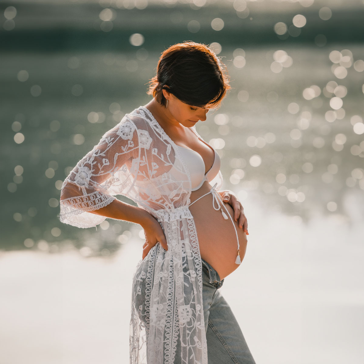Schwangere Frau im Gegenlicht am Wasser hält ihren Babybauch