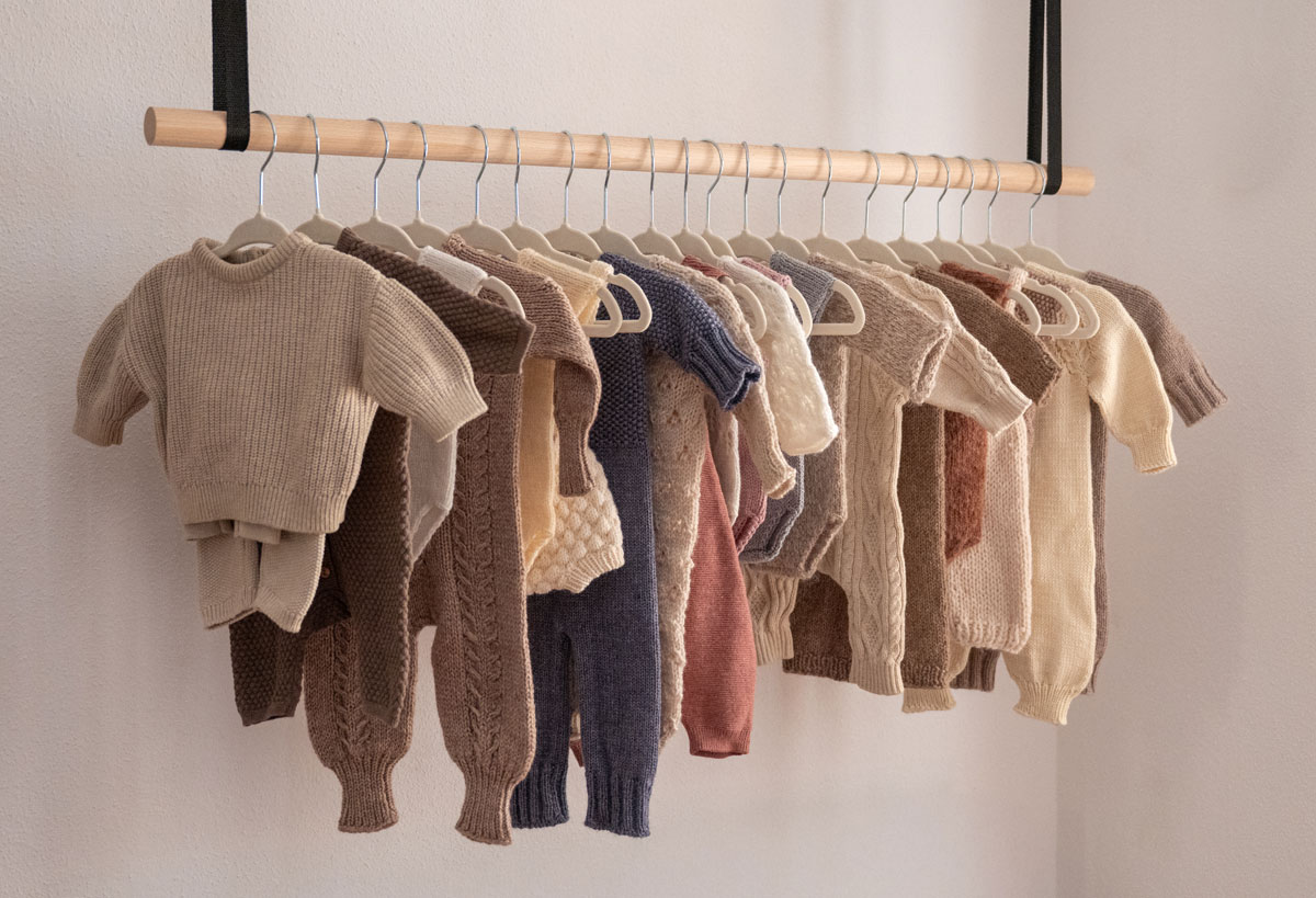 Handgestrickte Baby-Outfits in Naturtönen hängen an einer Holzstange im Fotostudio