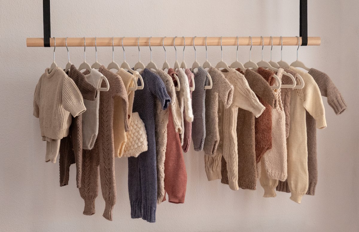 Handgestrickte Baby-Outfits in Naturtönen hängen an einer Holzstange im Fotostudio